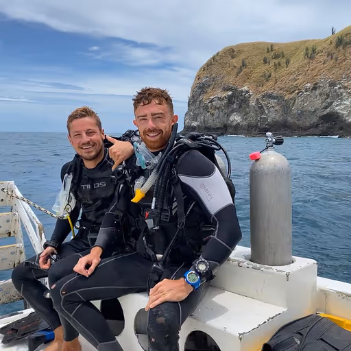 Maxime, the creator of Evasion Diving, on the scuba diving boat with a client, they are smiling for the picture
